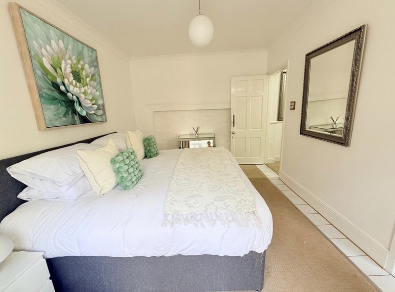 Bright bedroom with double bed, white bedding, green cushions, framed flower artwork and mirror