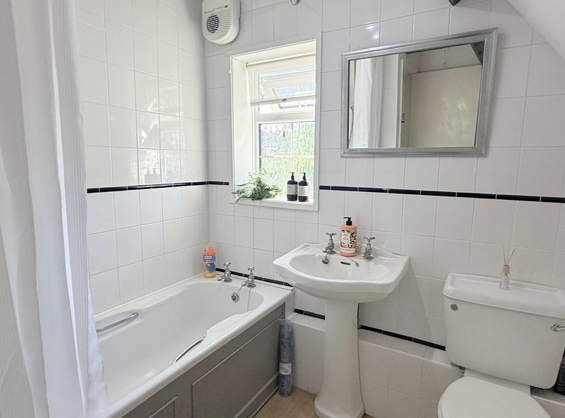 Clean bathroom with white tiles, bathtub, pedestal sink, mirror and window