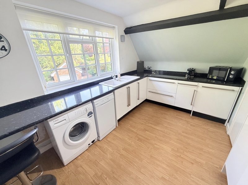 Modern kitchen with white cabinetry, dark countertop, washing machine, and large window overlooking garden