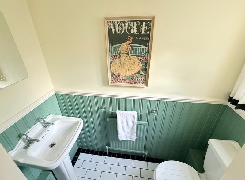 Bathroom with pedestal sink, toilet, and green panelled walls with vintage Vogue poster