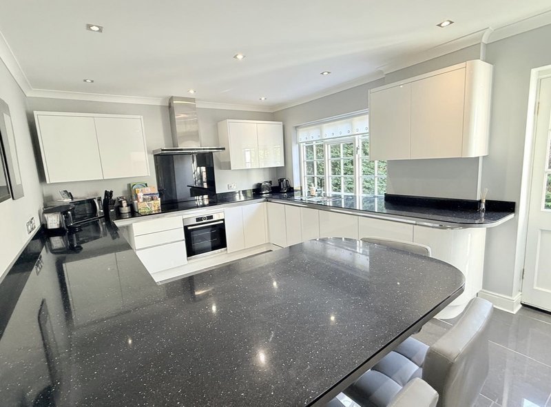 Modern kitchen with white cabinetry, grey stone countertops, built-in appliances and island seating