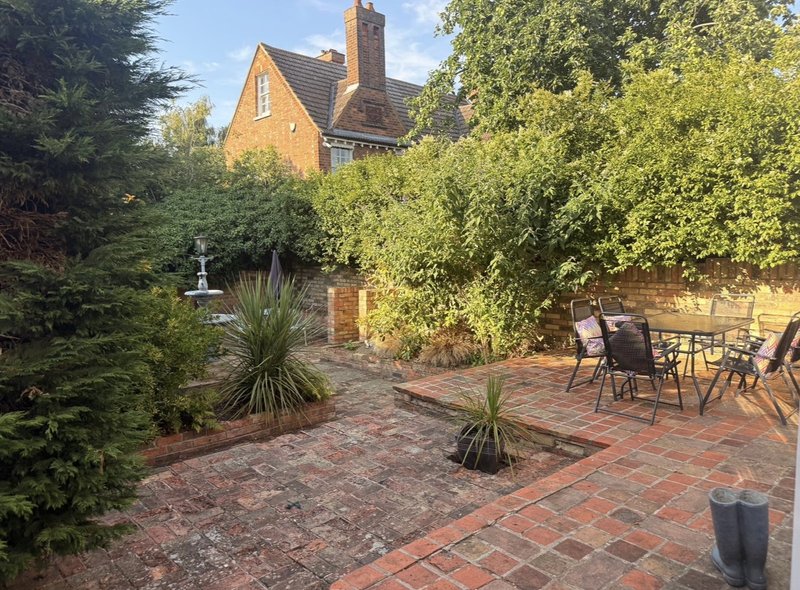 Brick patio with garden furniture, plants, and brick Victorian house in background