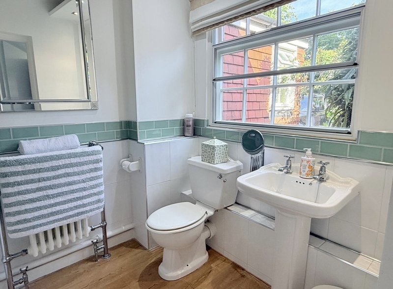 Bathroom with toilet, pedestal sink, heated towel rail and green tile accents