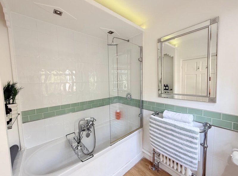 Modern bathroom with white subway tiles, green border stripe, bathtub with glass shower screen and heated towel rail