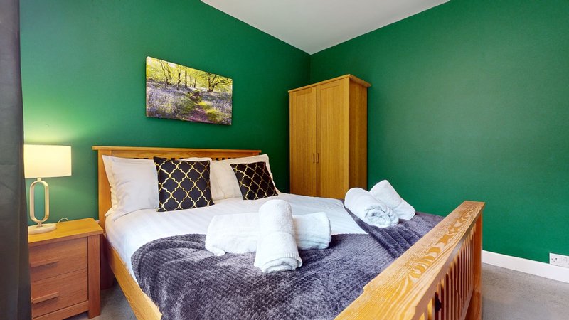 Bright bedroom with wooden bed, green walls, bedside lamp and framed artwork