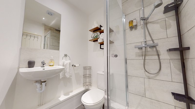 Modern bathroom with white tiles, walk-in shower, toilet, and wall-mounted sink
