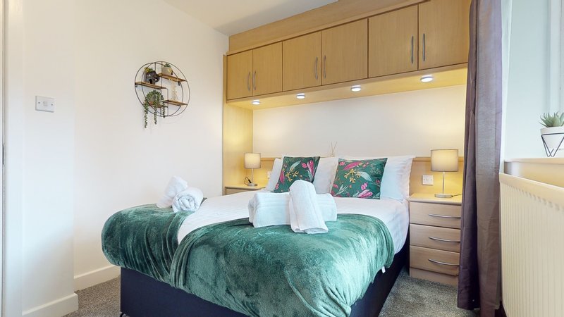 Modern bedroom with green velvet bed, built-in headboard with storage and lighting, decorative fan on wall