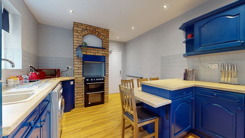 Modern kitchen with blue cabinets, yellow wooden floor, brick fireplace and dining table