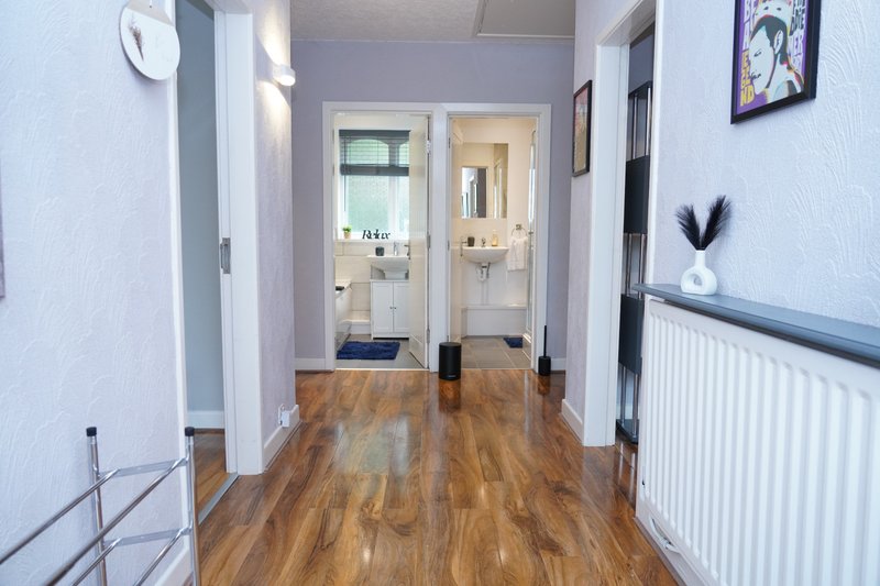 Hallway with wooden flooring, white walls, radiator and access to bathroom and kitchen areas