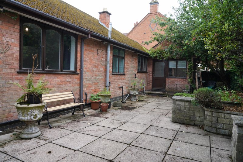 Red brick bungalow exterior with paved patio, seating area, planters and garden access