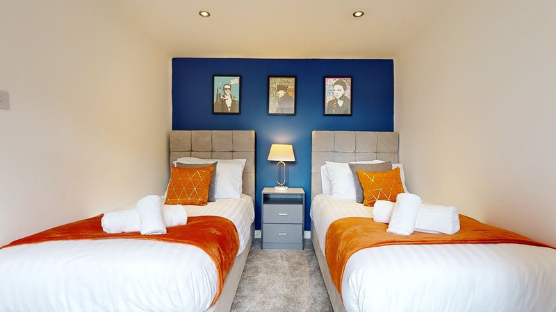 Twin bedroom with white bedding, orange blankets, blue headboard and framed wall art
