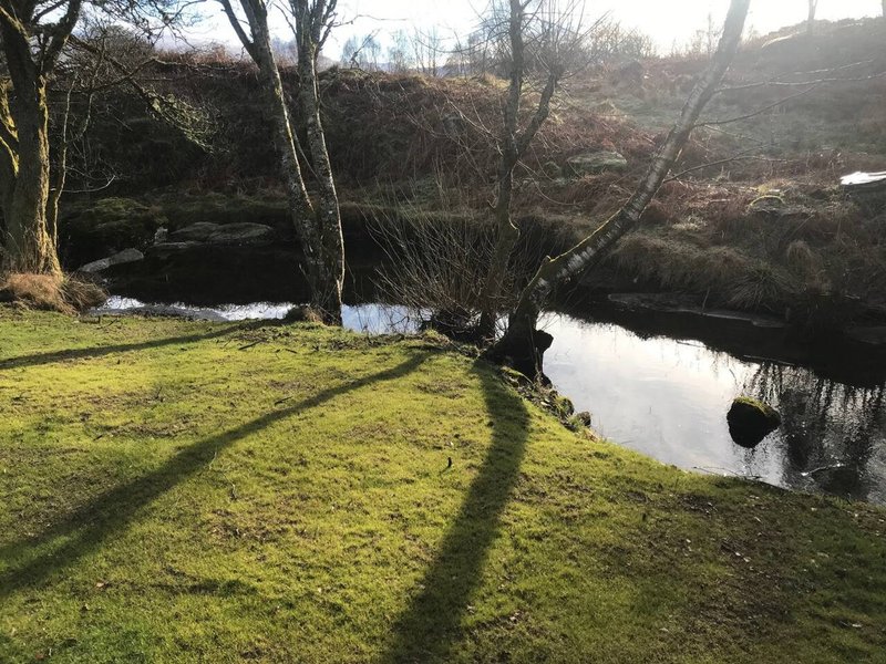 Garden grounds with stream, bare trees, grass lawn and hillside backdrop