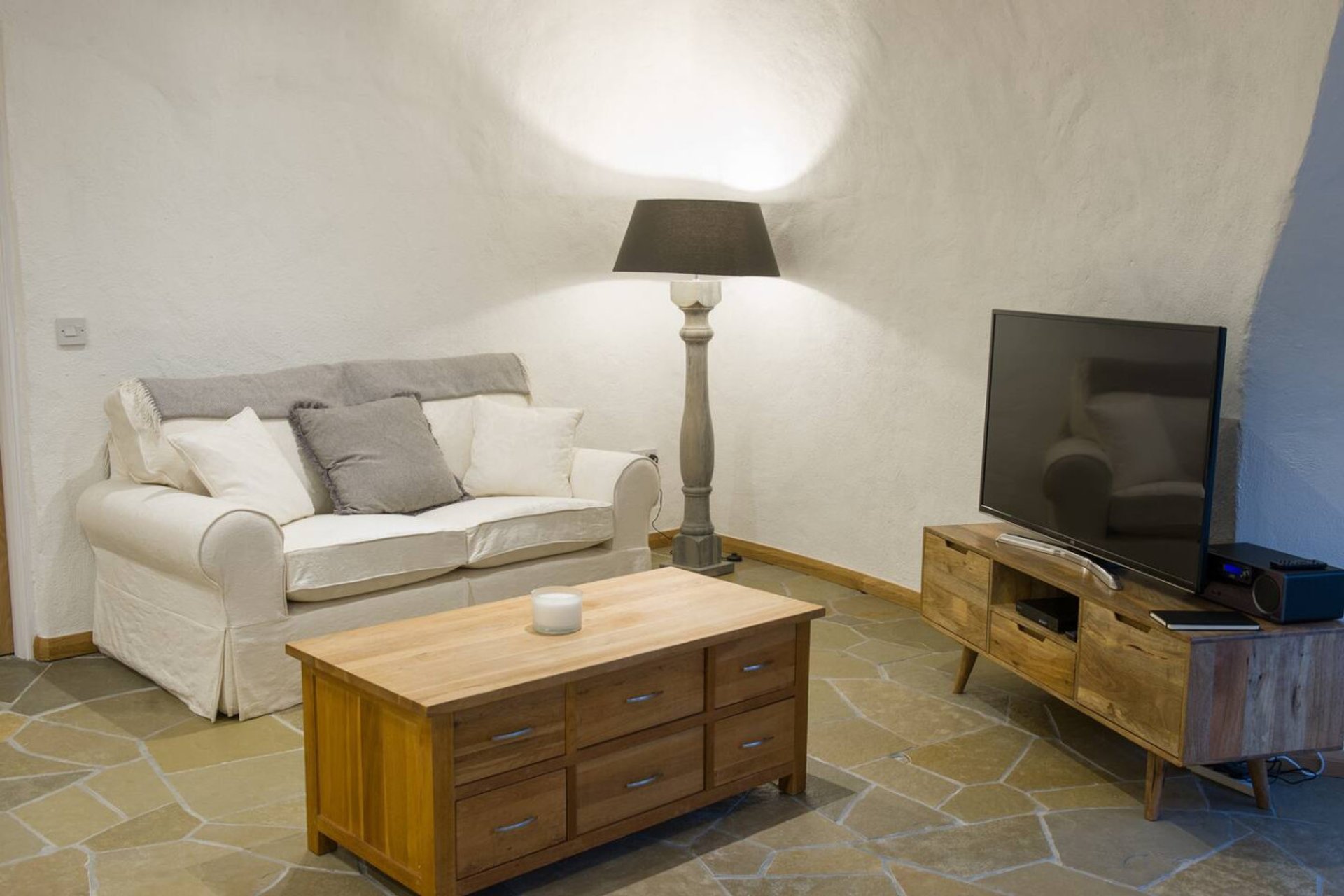Living room with cream sofa, wooden coffee table, TV unit, and table lamp