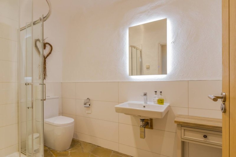 Modern bathroom with illuminated mirror, wall-mounted sink, toilet, and shower enclosure