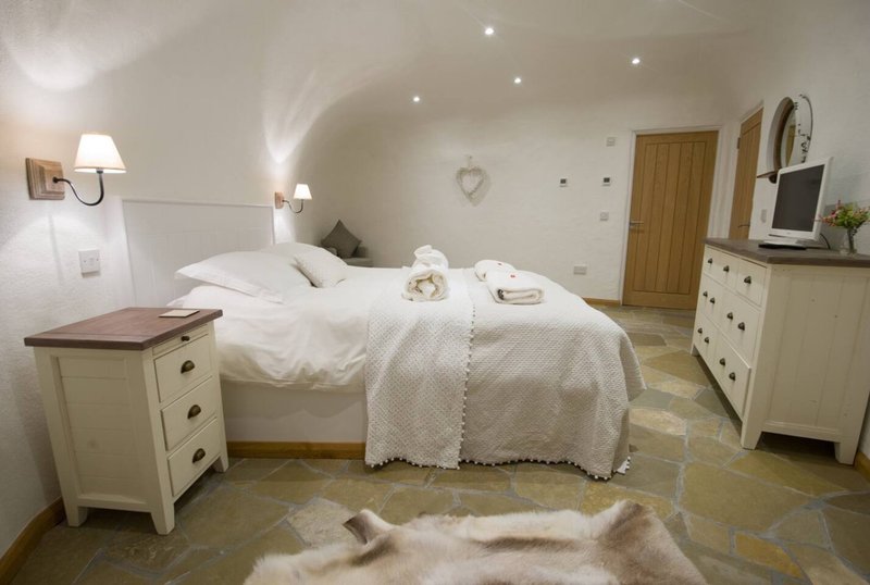 Spacious bedroom with white bedding, cream furniture, wooden doors and recessed ceiling lights