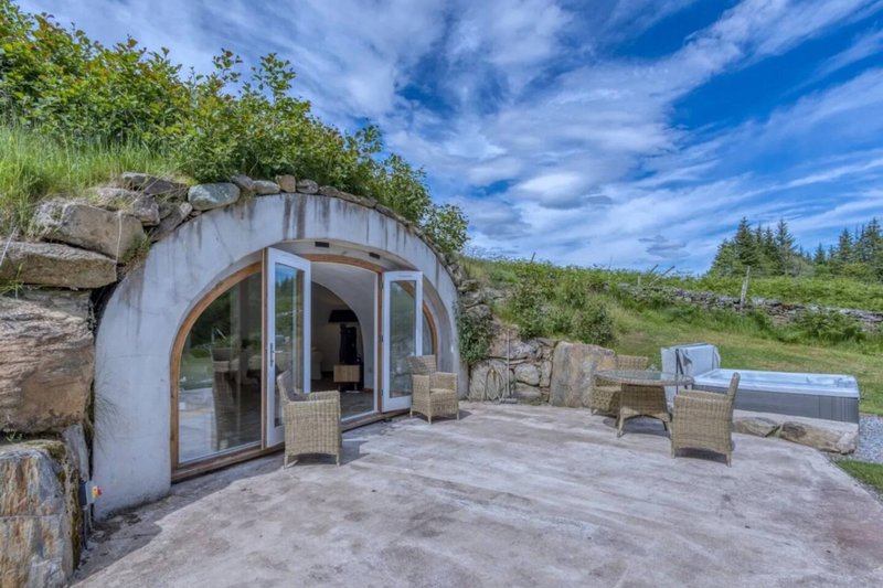 Modern curved pod accommodation with terrace, outdoor seating and natural landscape surroundings