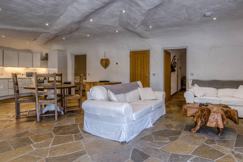Open-plan studio with white slipcover sofa, wooden dining table, kitchenette, stone flooring and exposed beams