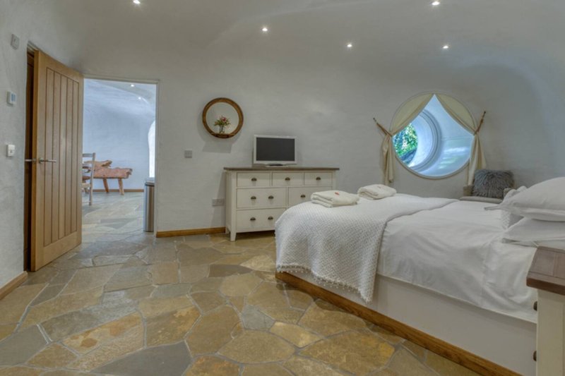 Bright bedroom with double bed, wooden furniture, porthole window, and stone flooring