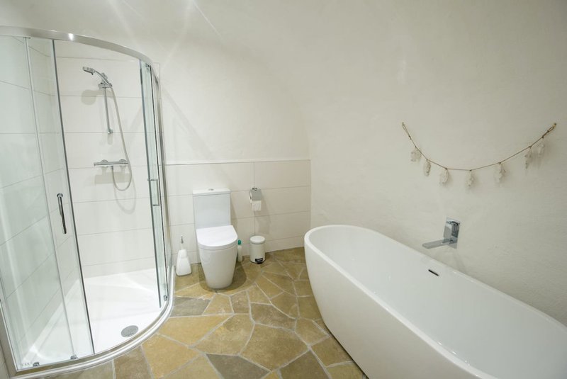 Modern bathroom with freestanding bathtub, curved shower enclosure, and natural stone flooring