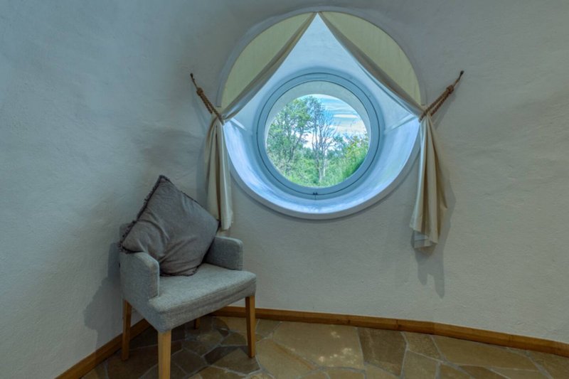 Minimalist bedroom corner with upholstered chair, round porthole window and wooden flooring