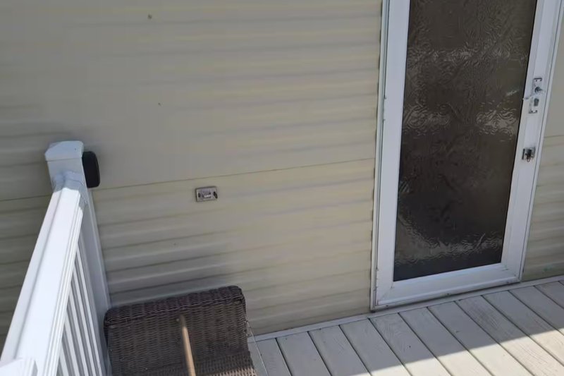 Exterior deck area with white railings, wicker chair, and glass door entry