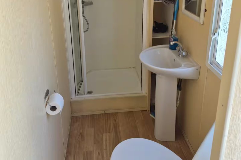 Small bathroom with toilet, pedestal sink, shower enclosure and wooden flooring