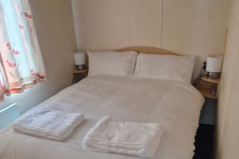 Bedroom with double bed, white bedding, folded towels, wooden bedside tables with lamps