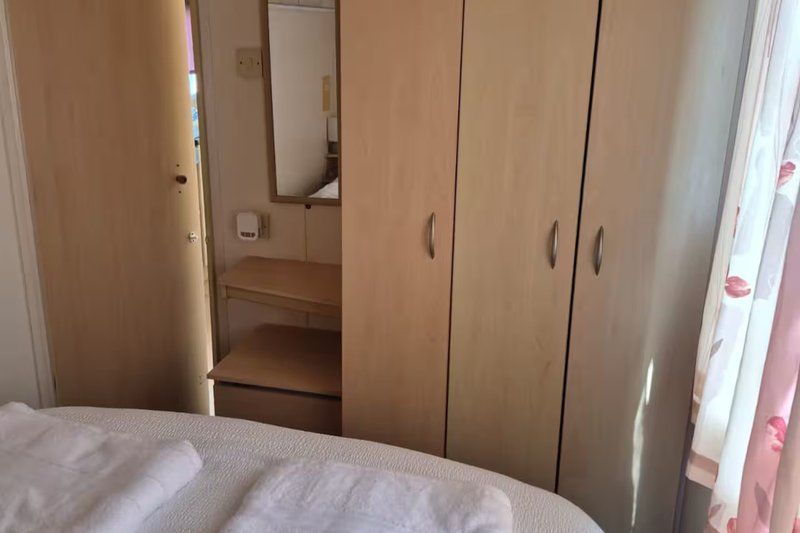Bedroom with double bed, wooden wardrobe, mirror and window with curtains