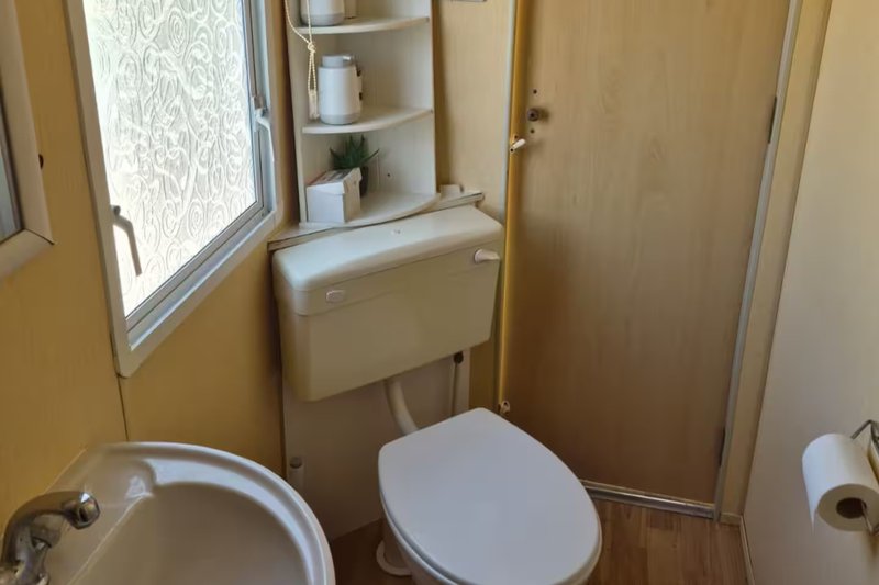 Small bathroom with toilet, sink, window, and wall-mounted storage shelves