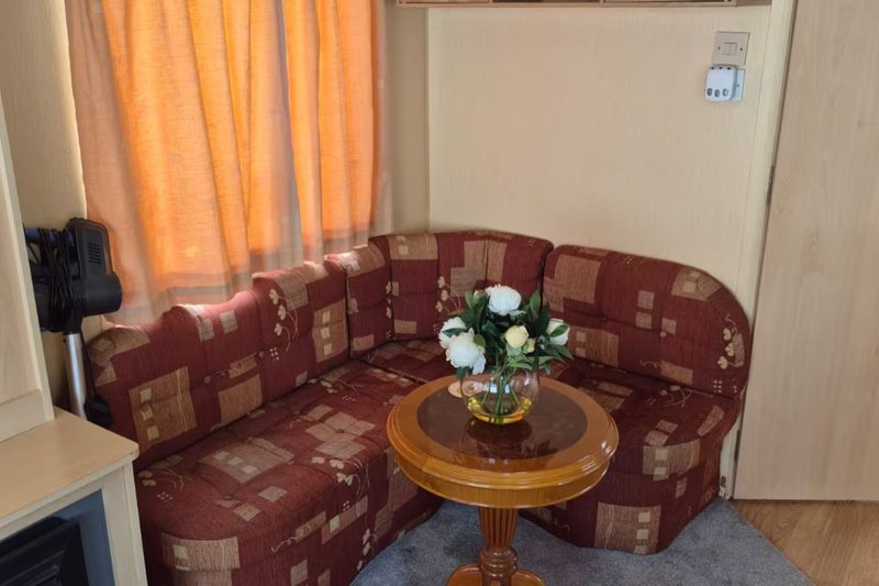 Living room corner with burgundy patterned sofa, round wooden table, white flowers, and orange curtains