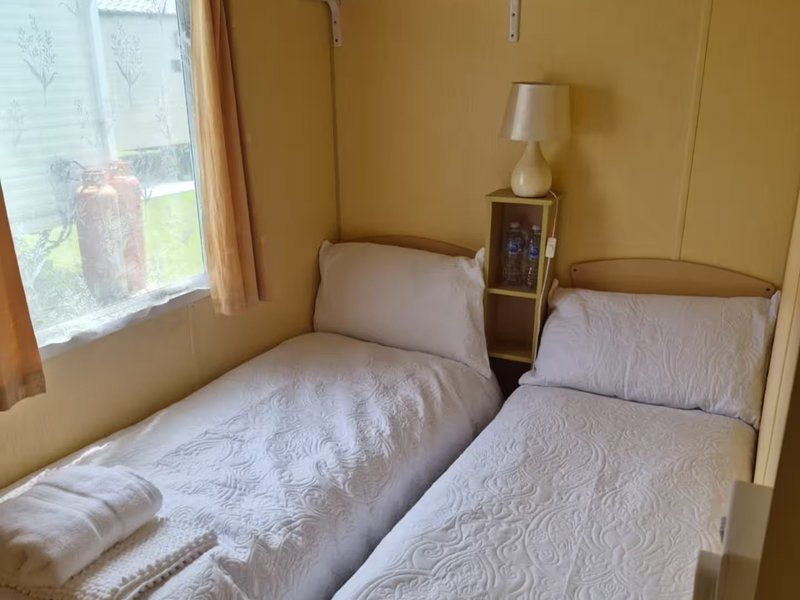 Twin bedroom with two single beds, bedside table, lamp, and window with garden view