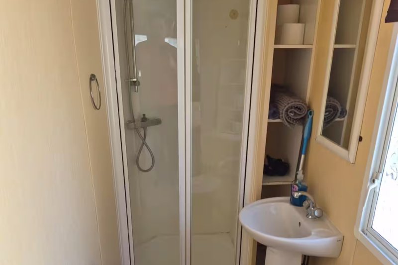 Bathroom with shower enclosure, corner sink, and storage shelving