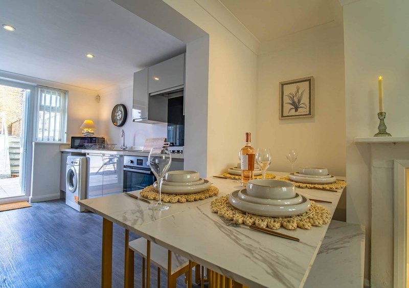Modern dining table with place settings, kitchen and laundry area visible in background