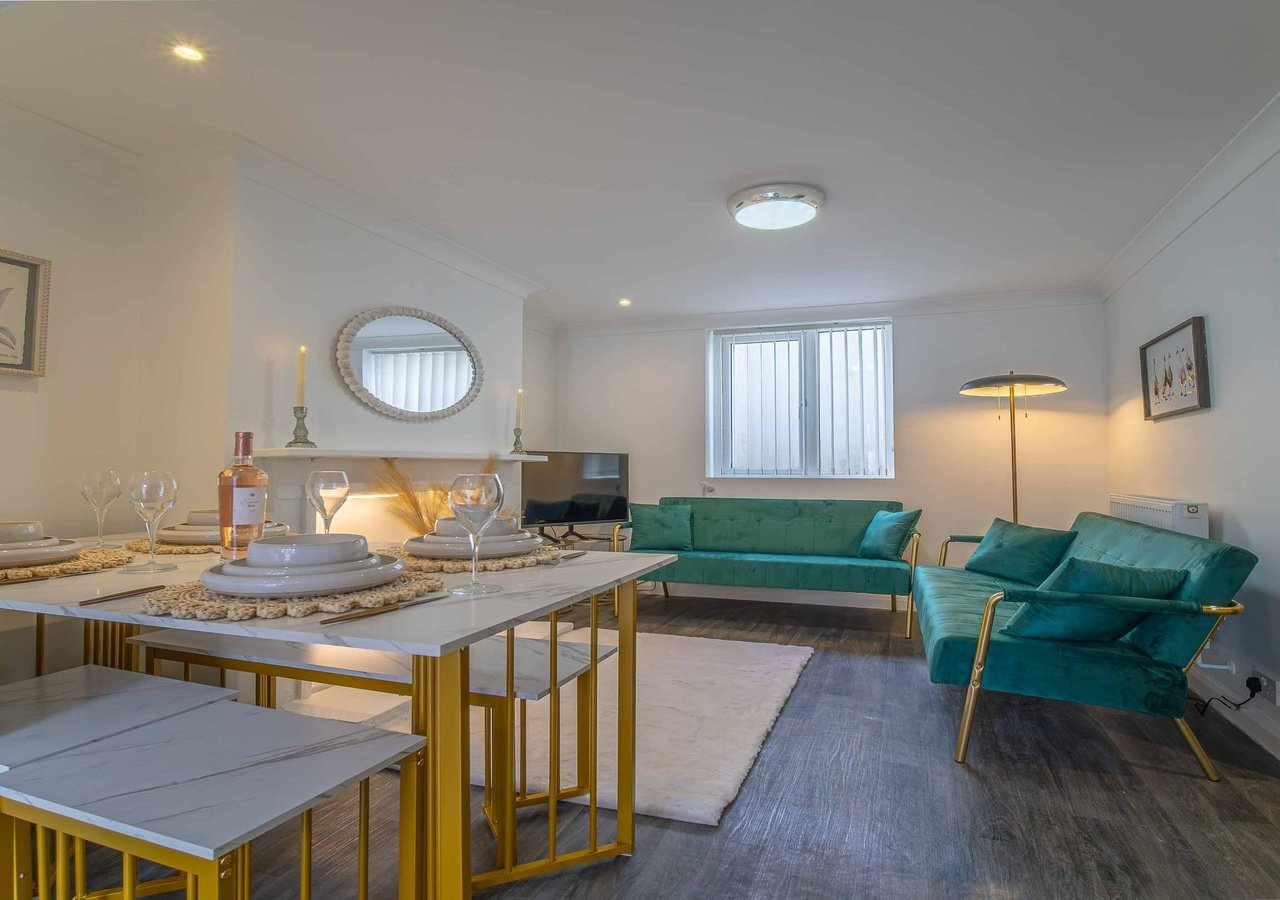 Open-plan living area with dining table, green upholstered sofa and armchairs, wooden flooring