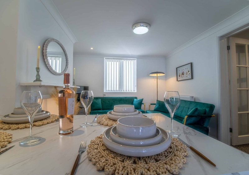Modern dining room with set table, wine glasses, bottle, and teal sofa in background
