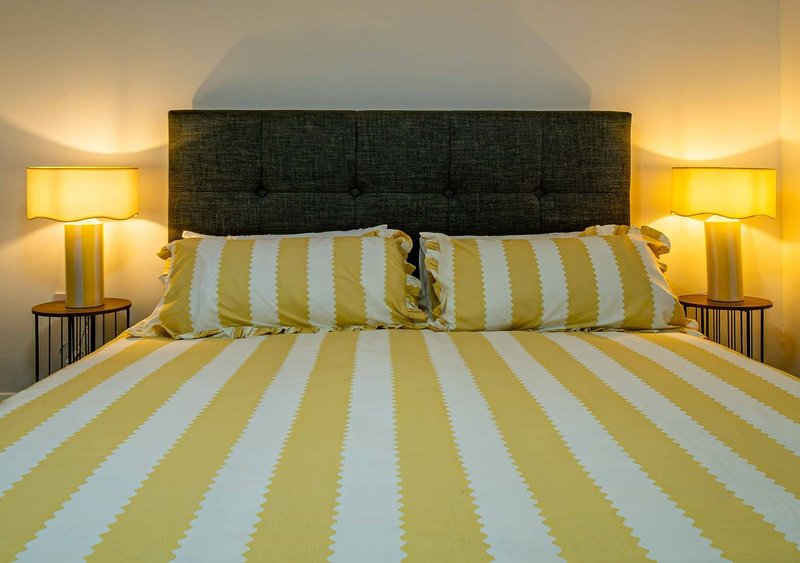 Bedroom with yellow and white striped bedding, dark headboard, and bedside lamps