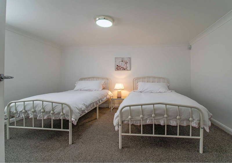 Twin bedroom with two white metal-frame beds, bedside lamp, and wall art