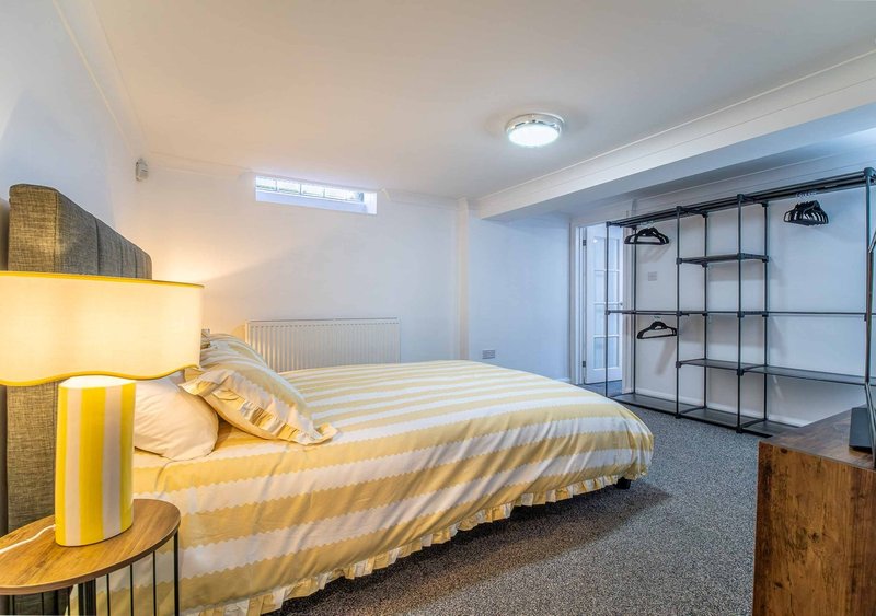 Bright bedroom with double bed, yellow bedding, shelving unit and recessed ceiling lights