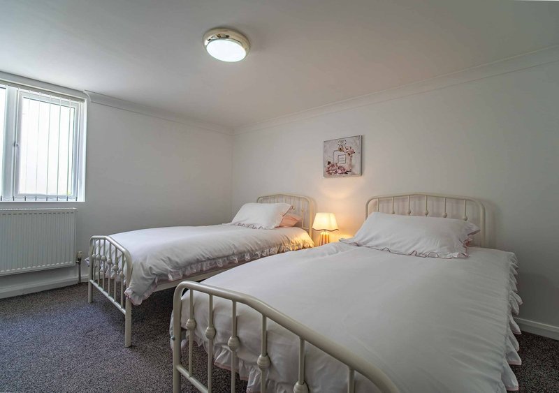 Bright bedroom with two single beds, metal frames, bedside lamp, and window with blinds