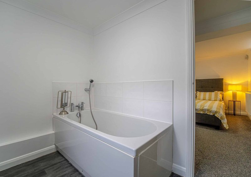 Modern bathroom with white freestanding bathtub, chrome fixtures, and view into adjacent bedroom with bed