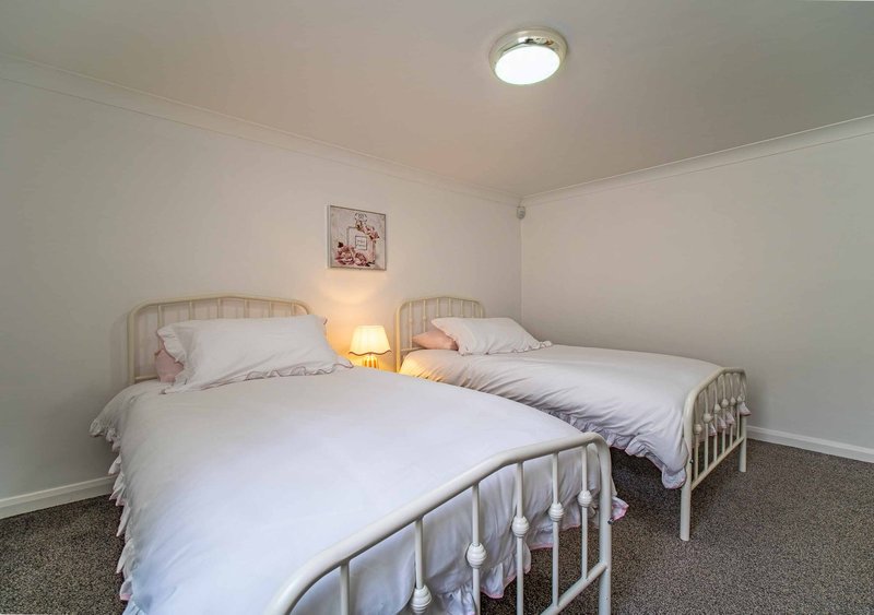 Bright bedroom with two single beds, metal frames, white bedding, and warm bedside lamp