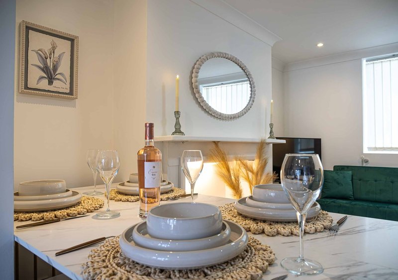 Dining table set for two with wine bottle, glasses, place settings and decorative mirror on wall