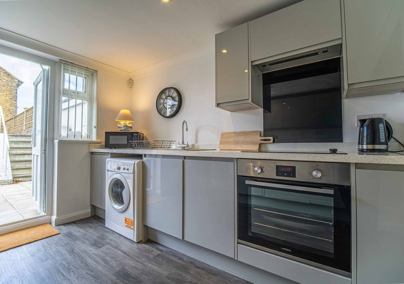 Modern kitchen with grey cabinets, integrated appliances, washing machine and patio door access