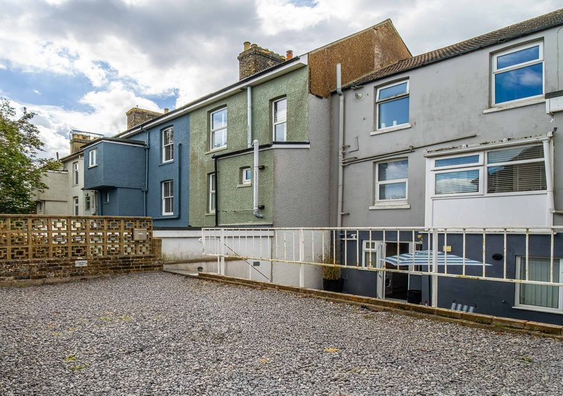 Multi-story residential building with blue and gray painted facades, gravel forecourt and metal railings