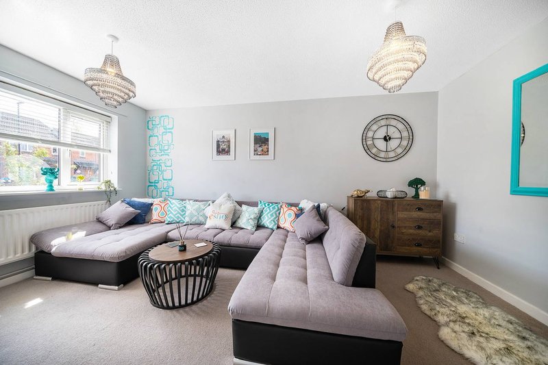 Bright living room with purple sectional sofa, decorative cushions, chandelier lighting, and wooden furniture
