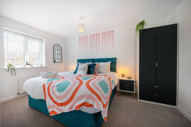 Bright bedroom with double bed, colorful bedding, teal headboard, black wardrobe and geometric wall art