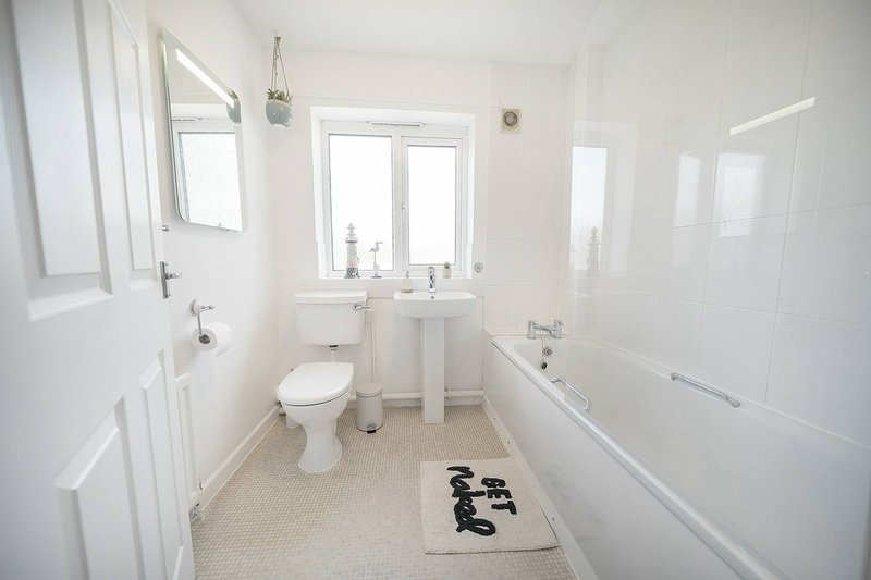 Bright modern bathroom with toilet, pedestal sink, bathtub and window