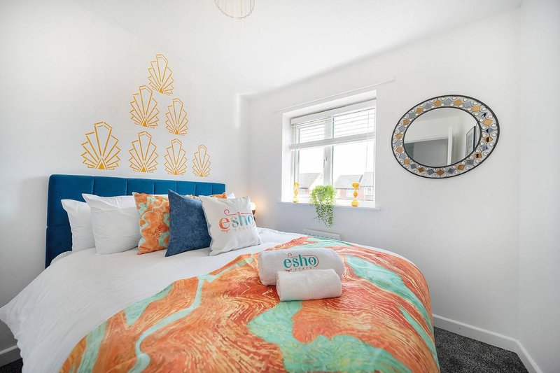 Bright bedroom with blue headboard, white bedding, orange patterned duvet, and gold wall art