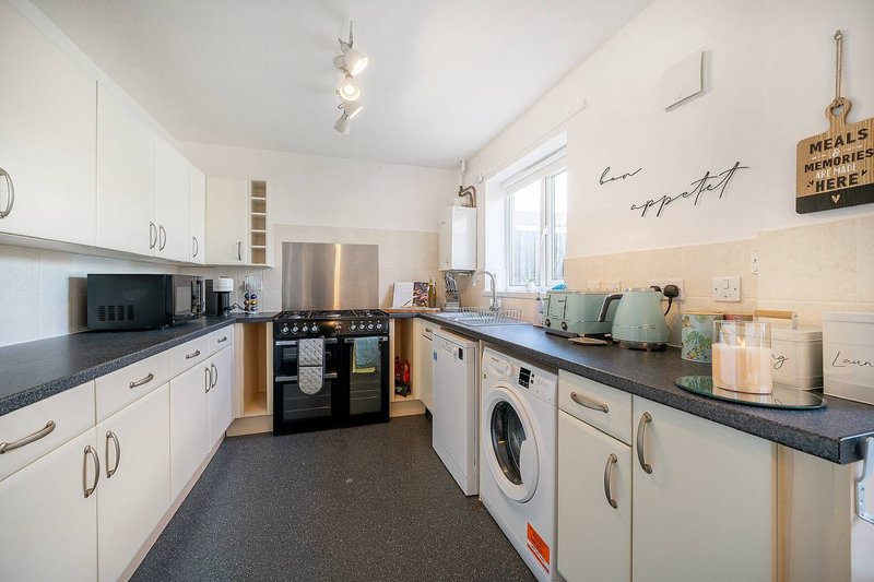 Modern kitchen with white cabinetry, black countertops, stainless steel appliances and washing machine