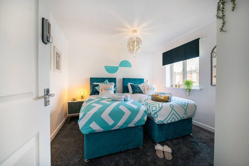 Bright bedroom with two single beds, turquoise bedding, pendant light and window with dark blind